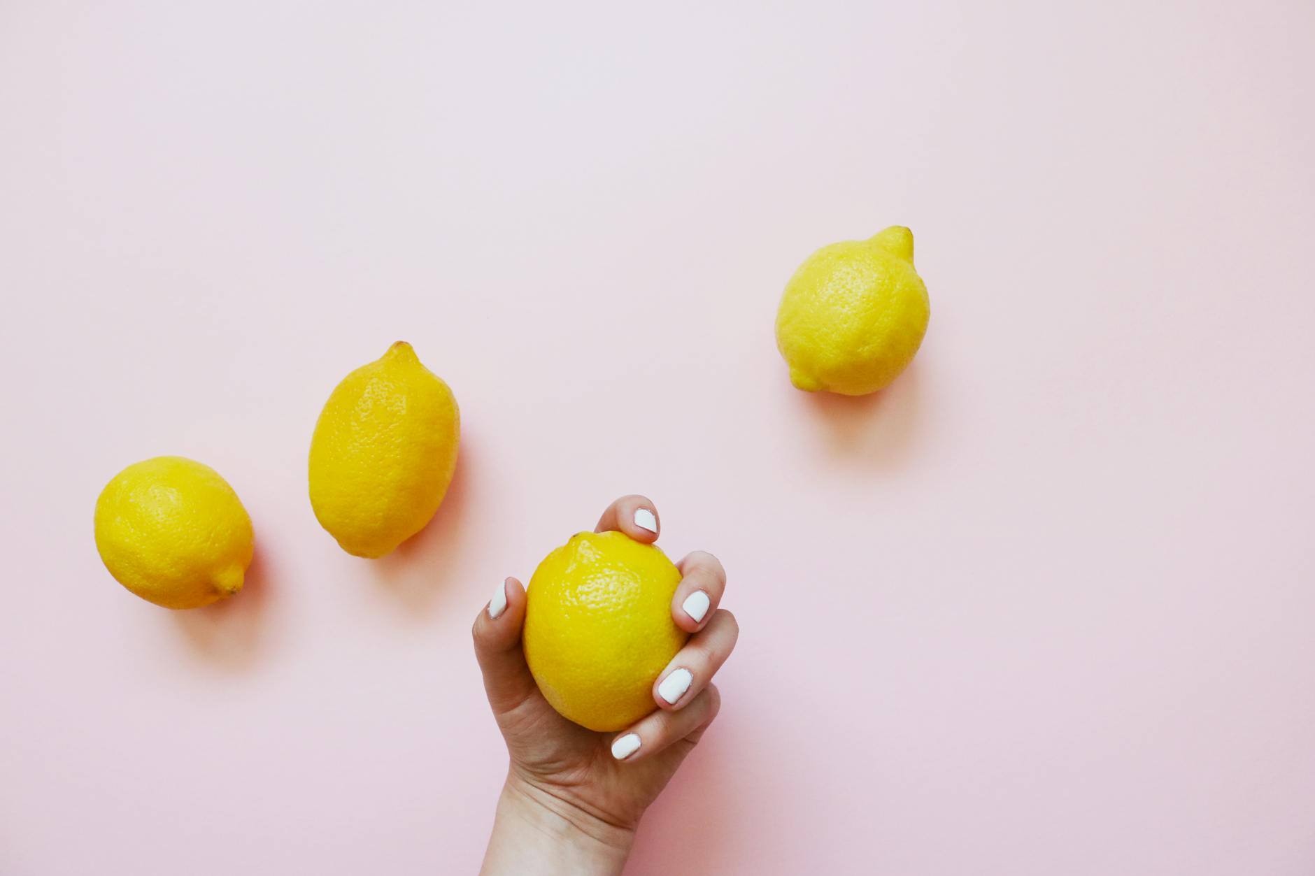 A hand holding a fresh lemon on a soft pink background, symbolizing new beginnings and renewed sensation